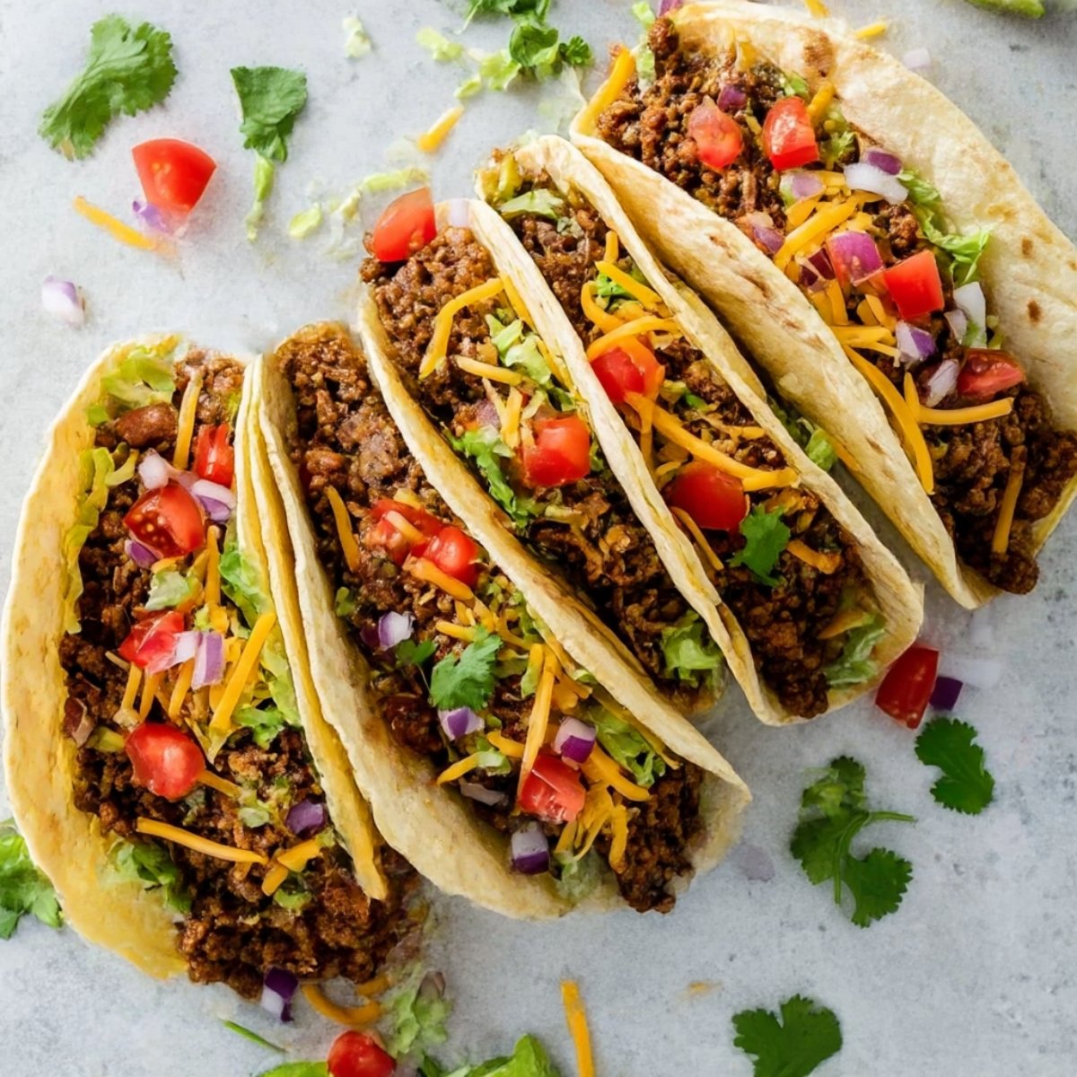Delicious ground beef soft tacos topped with shredded lettuce, cheddar cheese, diced tomatoes, and onions, served in soft flour tortillas, perfect for a quick and tasty meal.
