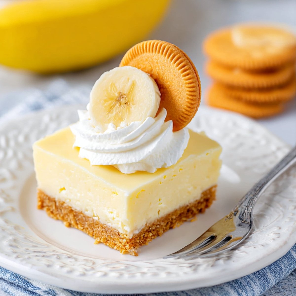 Delicious no-bake banana cheesecake slice topped with whipped cream, a banana slice, and a golden cookie on a white plate, perfect for easy homemade dessert recipes.