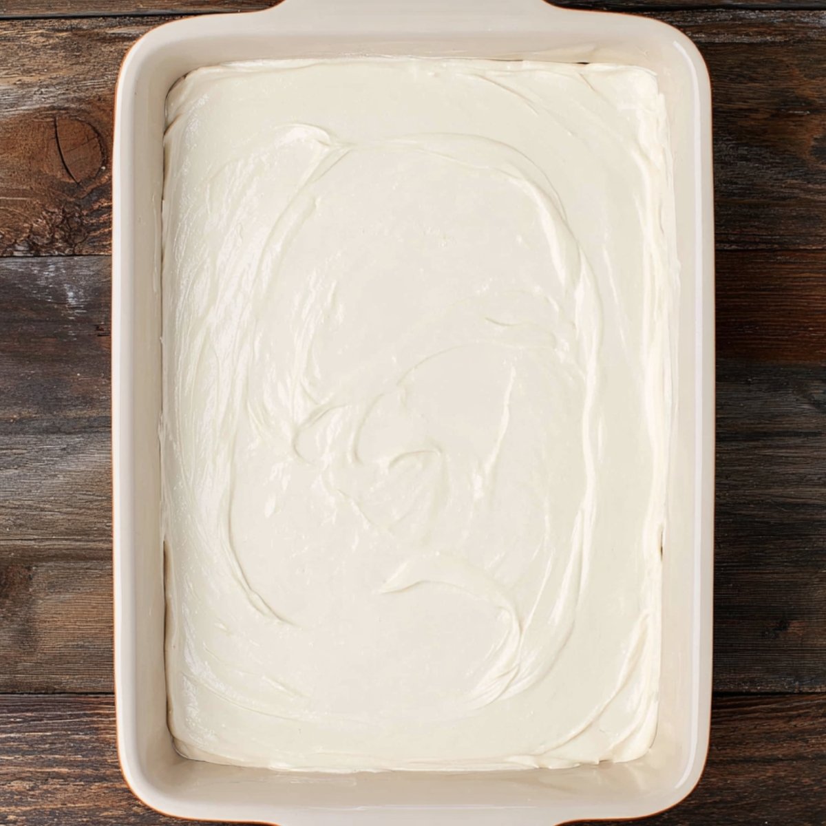 A baking dish filled with a smooth, creamy layer spread over a cookie crumb base, partway through making a Vanilla Lush Pie.